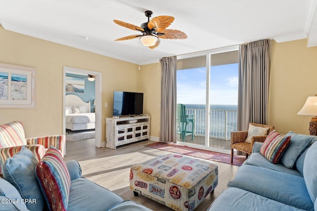 living area featuring expansive windows, ceiling fan, crown molding, and wood finished floors