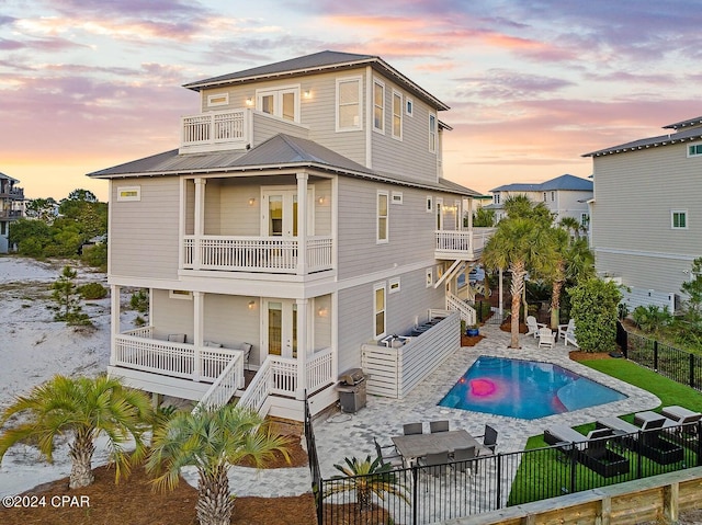 back house at dusk featuring a patio, a balcony, and a fenced in pool