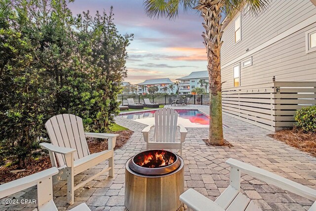 patio terrace at dusk with a fire pit and a fenced in pool