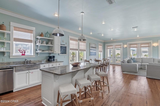 kitchen with french doors, white cabinets, stainless steel dishwasher, hanging light fixtures, and hardwood / wood-style floors