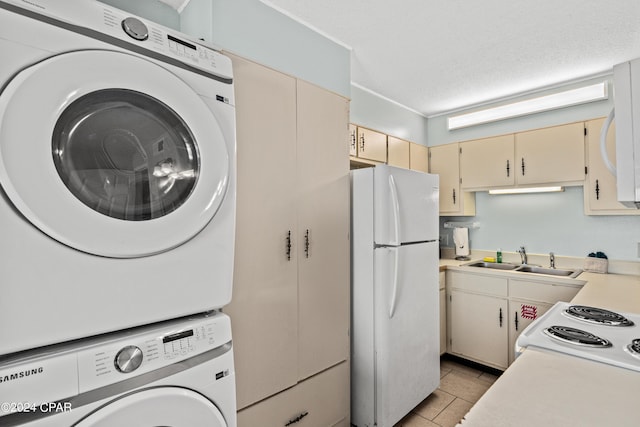 kitchen featuring stacked washer / drying machine, white refrigerator, sink, light tile patterned floors, and cream cabinetry