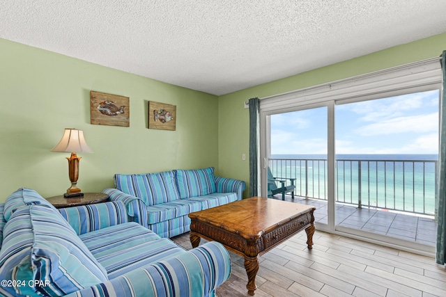 living room featuring light hardwood / wood-style floors, a water view, a textured ceiling, and a healthy amount of sunlight