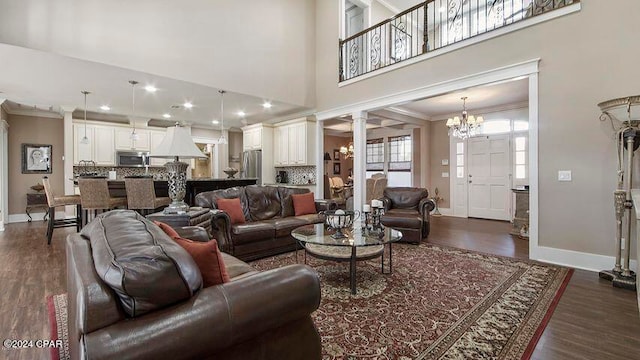 living room with a chandelier, decorative columns, dark hardwood / wood-style floors, ornamental molding, and a towering ceiling