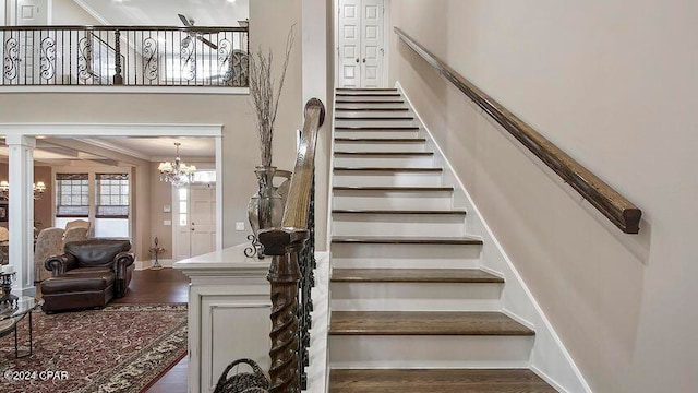 staircase with hardwood / wood-style floors, decorative columns, crown molding, and a notable chandelier