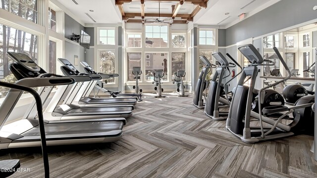 exercise room featuring a towering ceiling, coffered ceiling, and a healthy amount of sunlight