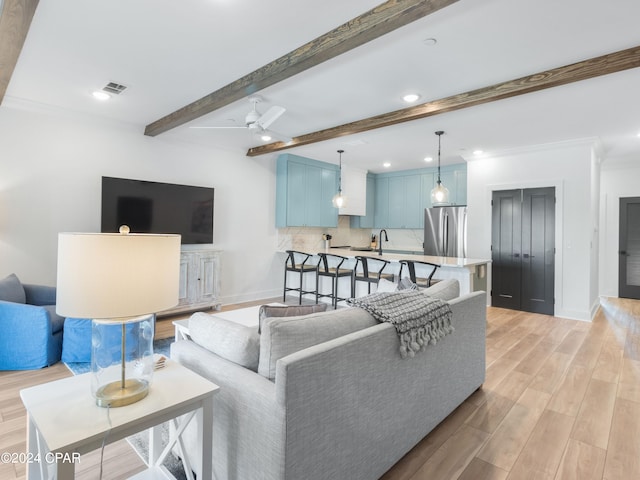 living room with ceiling fan, crown molding, beamed ceiling, and light wood-type flooring