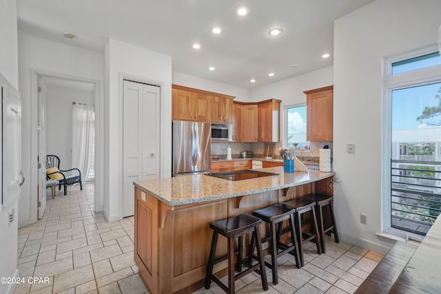 kitchen with backsplash, light stone countertops, a kitchen bar, kitchen peninsula, and stainless steel appliances