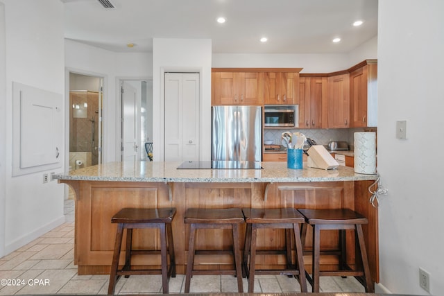 kitchen featuring kitchen peninsula, appliances with stainless steel finishes, light stone countertops, and a breakfast bar area