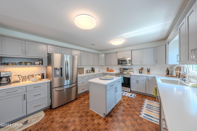 kitchen with appliances with stainless steel finishes, sink, a kitchen island, gray cabinetry, and tasteful backsplash