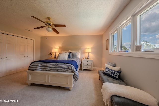 bedroom with a textured ceiling, a closet, light colored carpet, and ceiling fan