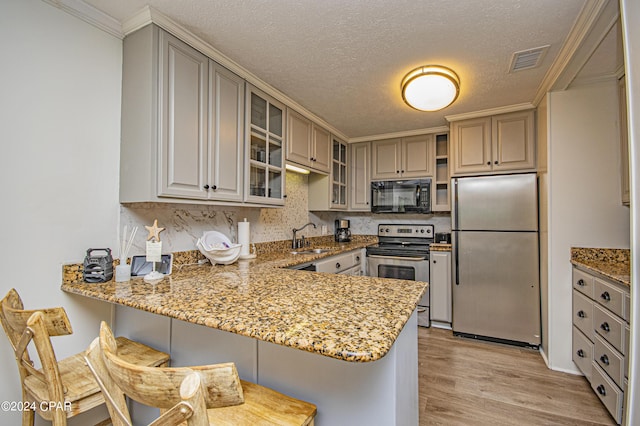 kitchen featuring sink, light hardwood / wood-style flooring, appliances with stainless steel finishes, a kitchen bar, and kitchen peninsula