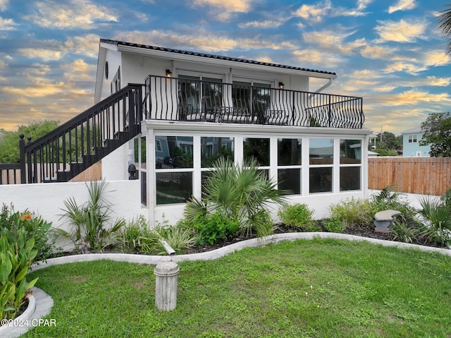 back house at dusk featuring a yard and a balcony