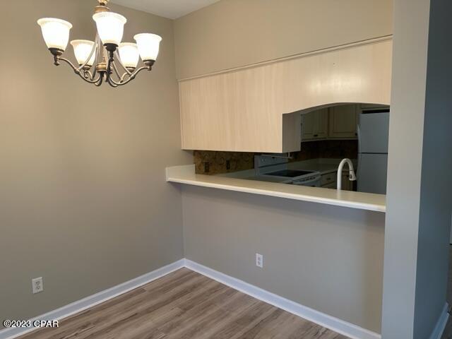 kitchen featuring white refrigerator, hanging light fixtures, wood-type flooring, electric stove, and a notable chandelier