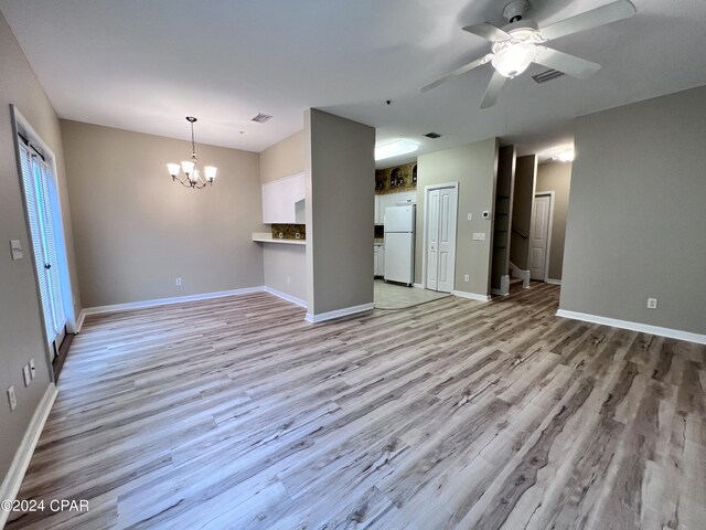 unfurnished living room with ceiling fan with notable chandelier and light hardwood / wood-style flooring