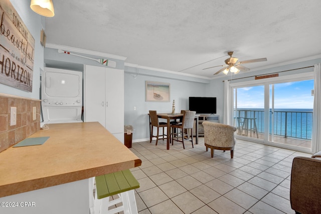 living room featuring ceiling fan, light tile patterned floors, crown molding, and stacked washer / dryer