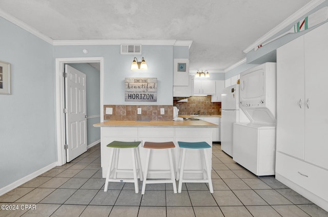 kitchen featuring light tile patterned flooring, stacked washer and clothes dryer, backsplash, white fridge, and white cabinetry