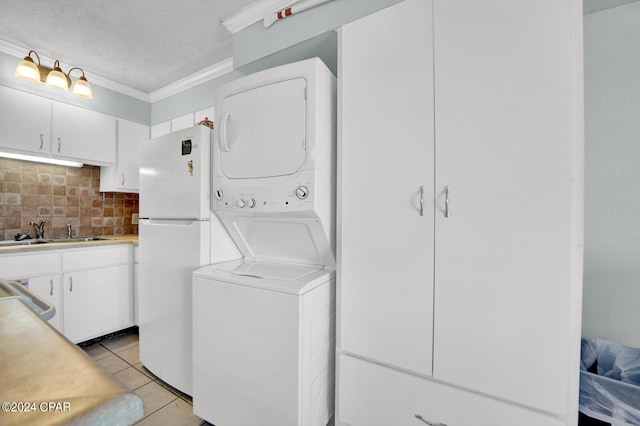 washroom with ornamental molding, light tile patterned floors, stacked washer and dryer, a textured ceiling, and sink