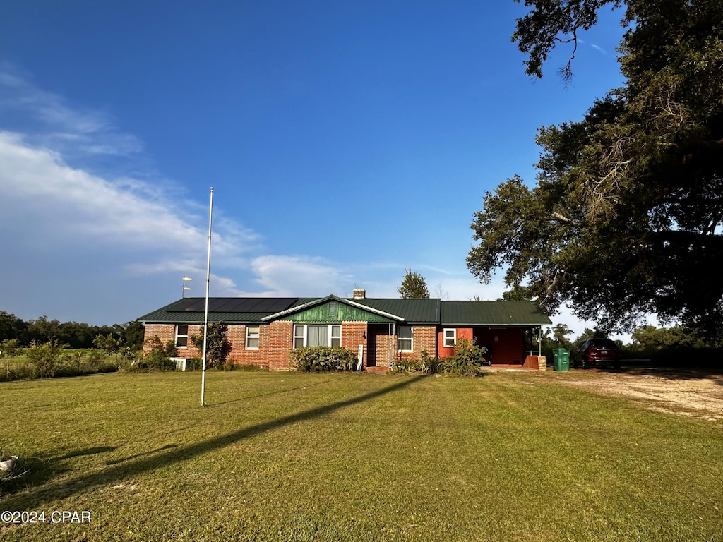 single story home with brick siding, solar panels, a front yard, a chimney, and driveway