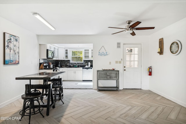 kitchen with dishwasher, decorative backsplash, light parquet flooring, white cabinets, and ceiling fan