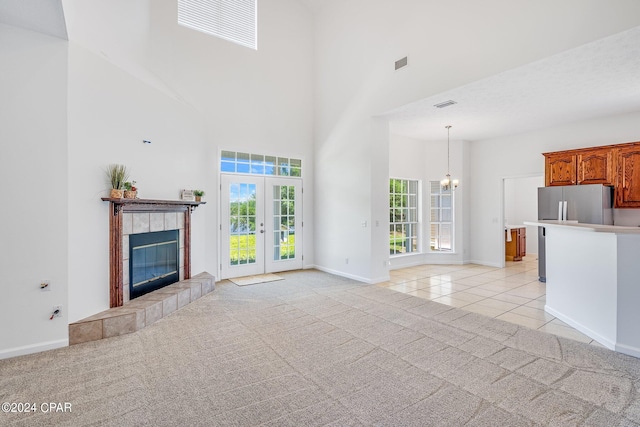 unfurnished living room with a chandelier, french doors, a high ceiling, a tiled fireplace, and light colored carpet