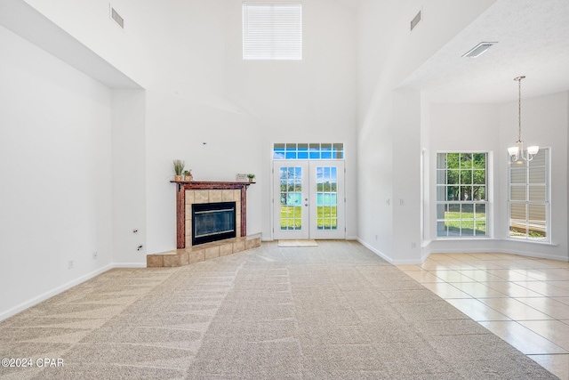 unfurnished living room featuring a high ceiling, a tile fireplace, french doors, a chandelier, and light colored carpet