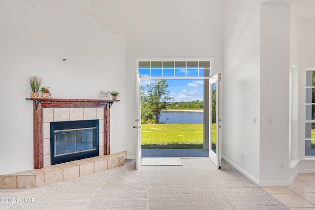 unfurnished living room featuring a tiled fireplace, light colored carpet, and a water view