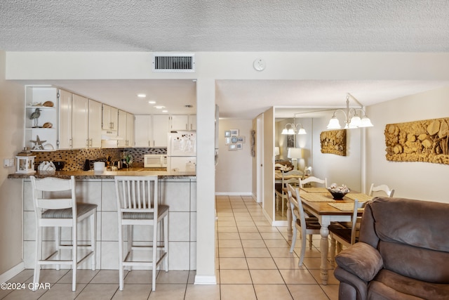 kitchen featuring light tile patterned flooring, white cabinetry, a breakfast bar area, white appliances, and decorative backsplash