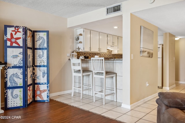 kitchen with white cabinets, white refrigerator, light hardwood / wood-style floors, backsplash, and a textured ceiling