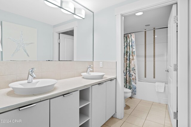 full bathroom with toilet, tile patterned floors, shower / tub combo with curtain, dual bowl vanity, and decorative backsplash