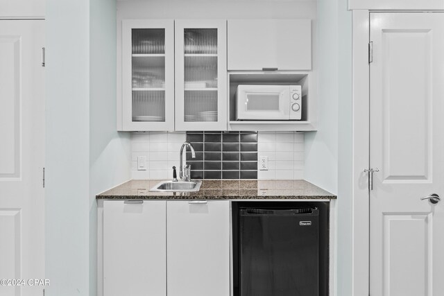 bar featuring white microwave, sink, black dishwasher, and white cabinetry