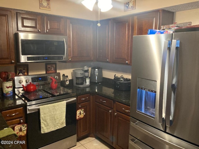 kitchen with dark stone counters, dark brown cabinets, ceiling fan, appliances with stainless steel finishes, and light tile patterned floors