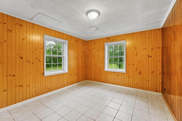 tiled empty room featuring wooden walls, ornamental molding, and a healthy amount of sunlight