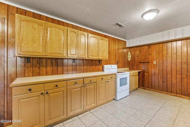 kitchen featuring light tile patterned floors, wooden walls, tile counters, and electric range