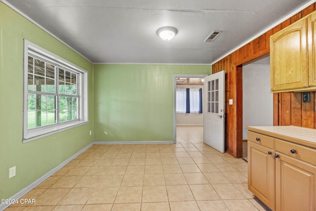 kitchen with wood walls, light brown cabinetry, light tile patterned floors, and crown molding