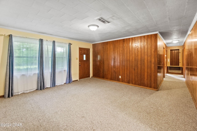 carpeted spare room with crown molding and wood walls