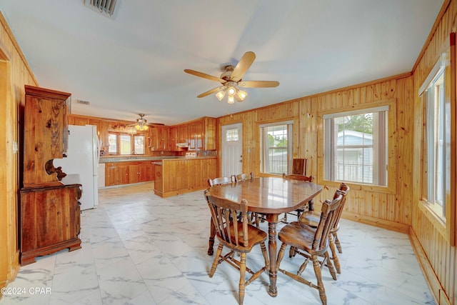 tiled dining room featuring ceiling fan and wood walls