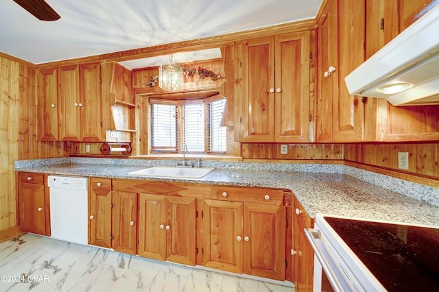 kitchen with light tile patterned floors, white dishwasher, wooden walls, sink, and light stone counters