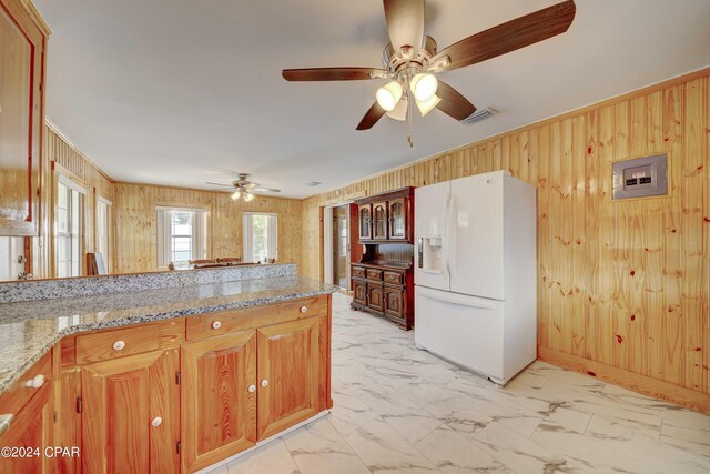 kitchen with white fridge with ice dispenser, light tile patterned flooring, light stone counters, ceiling fan, and wood walls