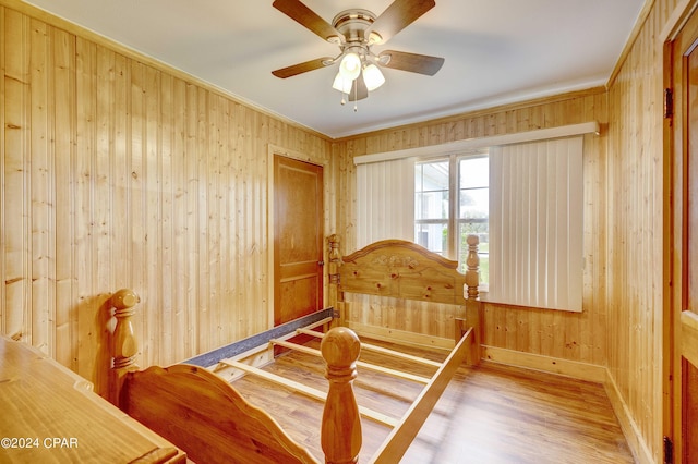 bedroom featuring ceiling fan, wooden walls, ornamental molding, and wood-type flooring