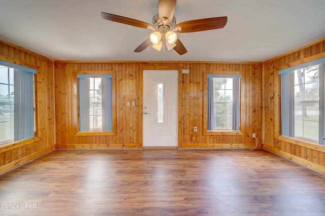 foyer entrance with ceiling fan, wood walls, wood-type flooring, and a healthy amount of sunlight