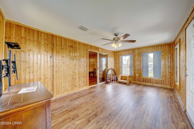 unfurnished living room featuring ceiling fan, wood walls, and wood-type flooring