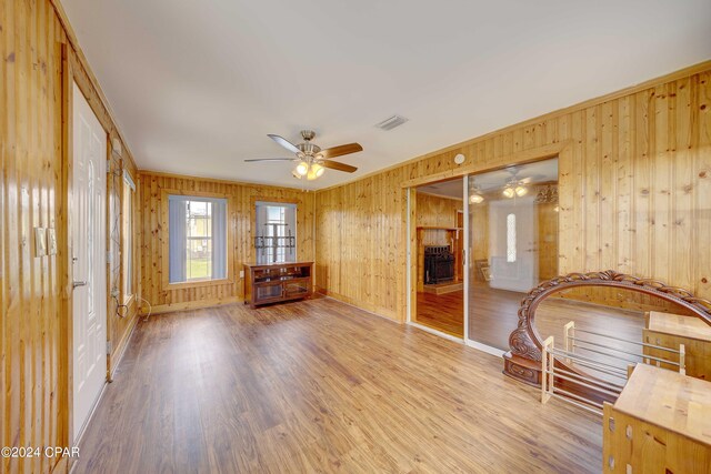 unfurnished living room with ceiling fan, light hardwood / wood-style flooring, and wooden walls