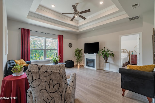 living room with ceiling fan, a tray ceiling, and light wood-type flooring