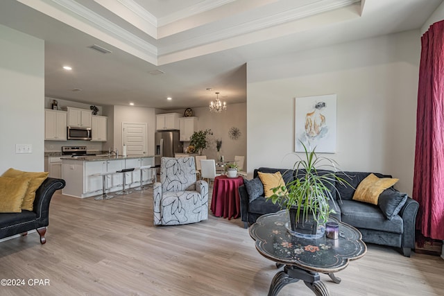 living room featuring an inviting chandelier, a tray ceiling, ornamental molding, light hardwood / wood-style flooring, and sink