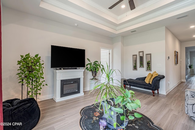 living room featuring light wood-type flooring, a tray ceiling, and ornamental molding