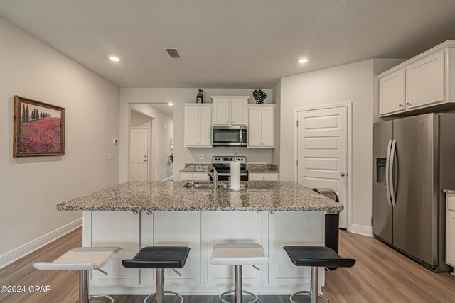 kitchen featuring appliances with stainless steel finishes, white cabinets, light stone counters, and a kitchen island with sink