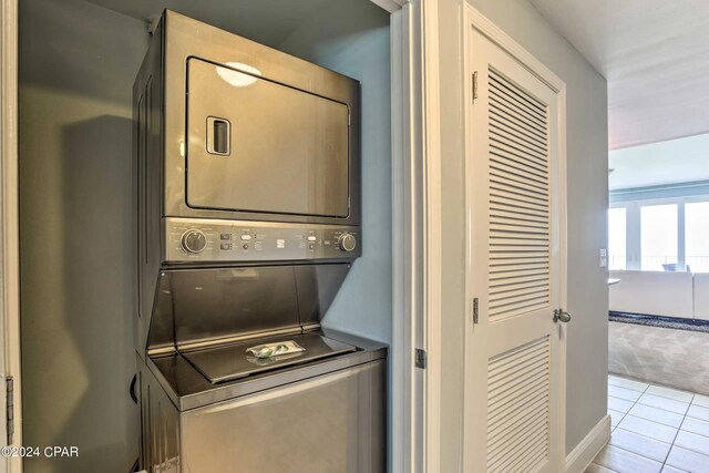 laundry area with stacked washing maching and dryer and light tile patterned floors