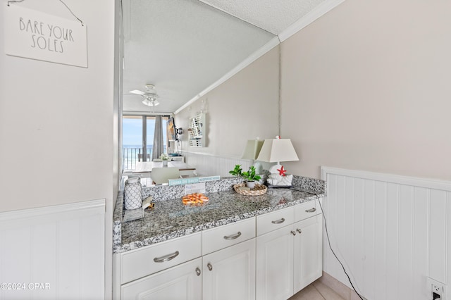 kitchen featuring white cabinets, a textured ceiling, ceiling fan, dark stone counters, and ornamental molding