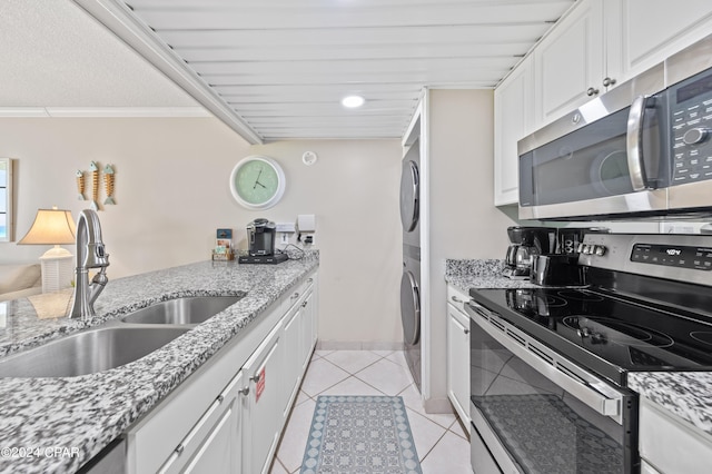 kitchen featuring appliances with stainless steel finishes, white cabinetry, crown molding, stacked washer and dryer, and sink