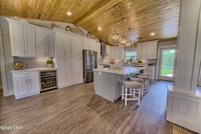 kitchen with wooden ceiling, beverage cooler, a breakfast bar, freestanding refrigerator, and wall chimney exhaust hood